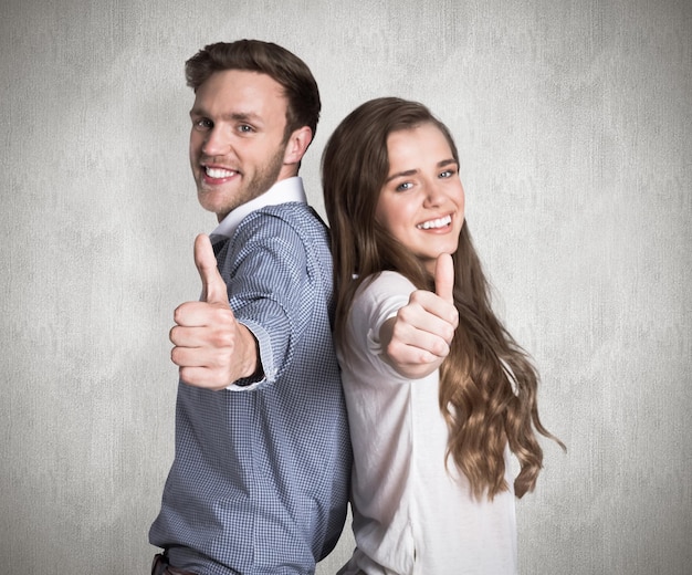 Casal jovem feliz gesticulando polegares contra a superfície resistida