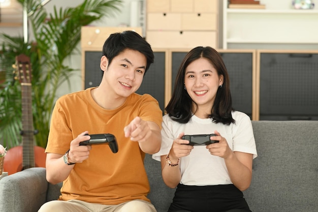 Casal jovem feliz jogando videogame com joysticks enquanto está sentado no sofá na sala de estar