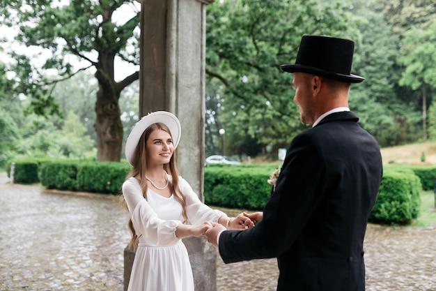 Casal jovem feliz Noivas de chapéu Moça em um vestido de noiva branco e chapéu com um buquê de flores Noivas no castelo Noiva e noivo