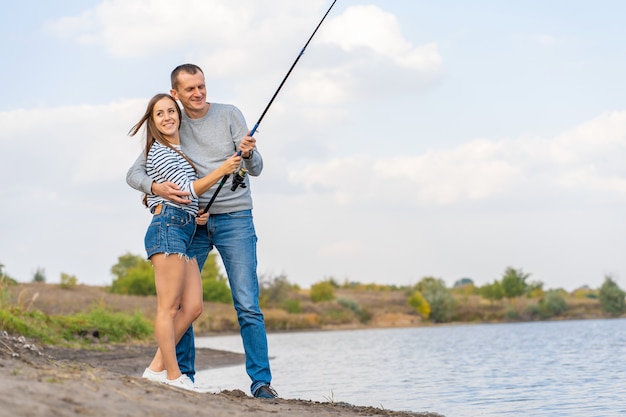 Casal jovem feliz pesca à beira do lago