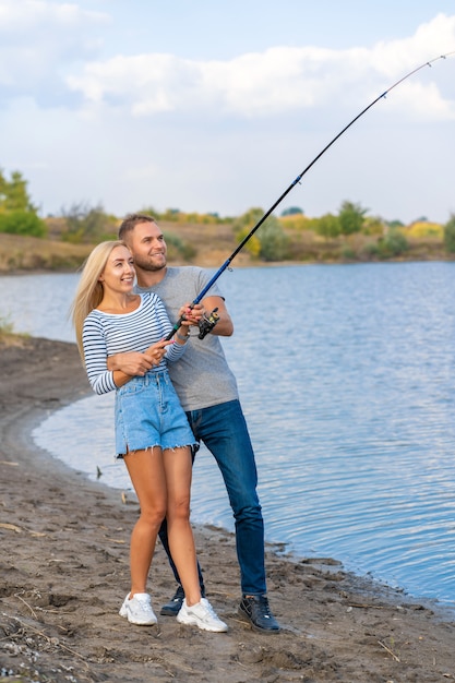 Casal jovem feliz pesca à beira do lago