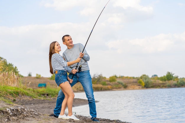 Casal jovem feliz pesca à beira do lago