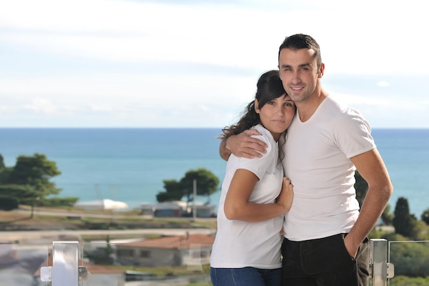 casal jovem feliz relaxa na varanda ao ar livre com oceano e céu azul ao fundo