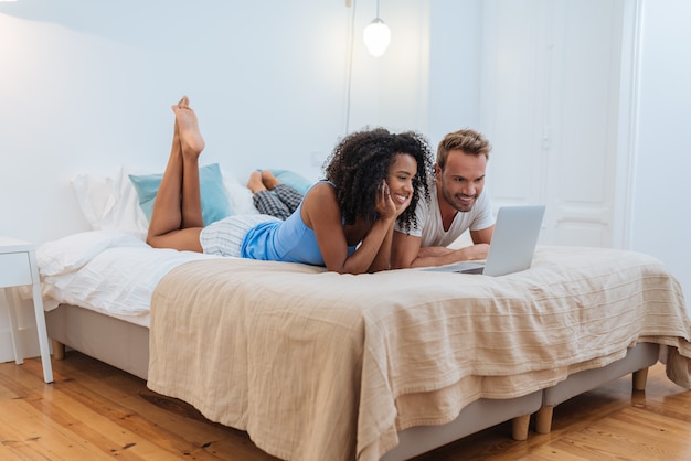 Casal jovem feliz relaxado em casa deitado na cama no computador