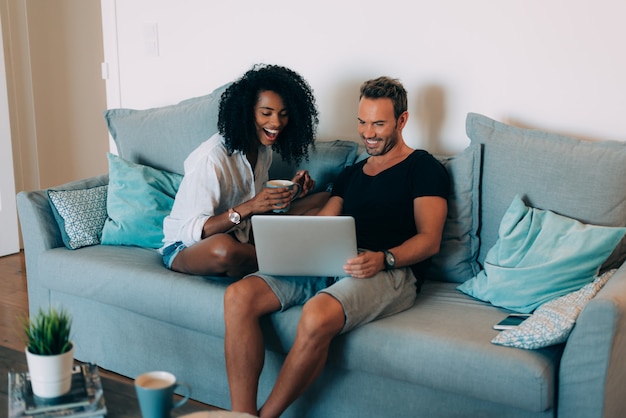 Casal jovem feliz relaxado em casa no sofá no telefone celular e computador