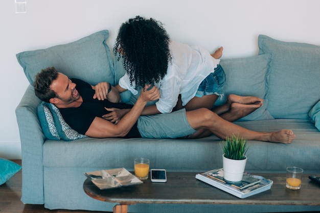 Casal jovem feliz relaxado em casa no sofá se divertindo brincando uns com os outros