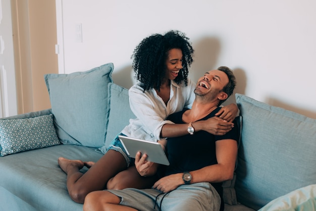 Casal jovem feliz relaxado em casa sentado no sofá sobre o tablet