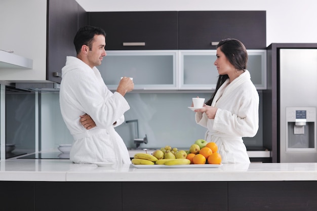 casal jovem feliz se diverte na cozinha moderna interior enquanto prepara frutas frescas e salada de legumes