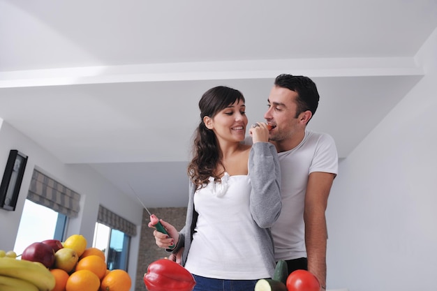 casal jovem feliz se diverte na cozinha moderna interior enquanto prepara frutas frescas e salada de legumes