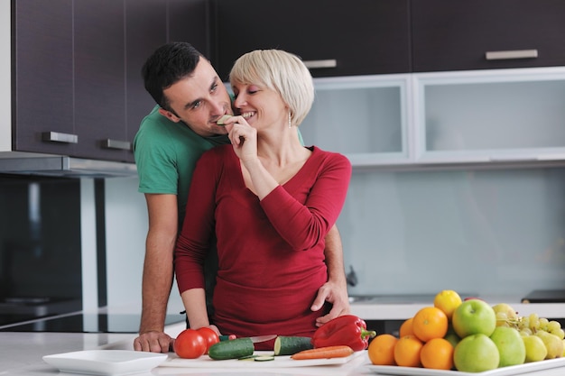 casal jovem feliz se diverte na cozinha moderna interior enquanto prepara frutas frescas e salada de legumes