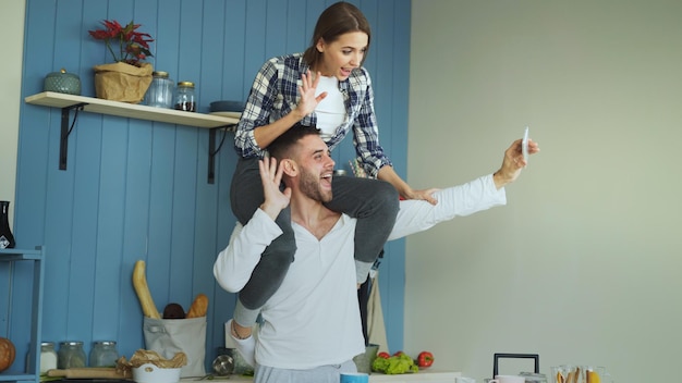 Casal jovem feliz se divertindo e conversando por videochamada online na cozinha em casa