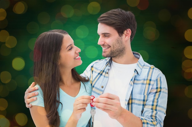 Casal jovem feliz segurando a nova chave da casa contra o fechamento das luzes de natal