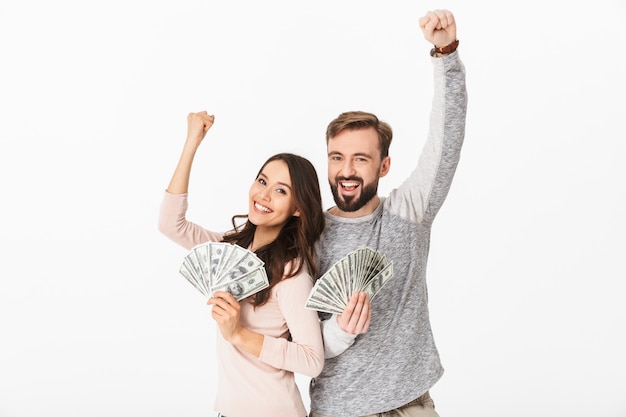 Casal jovem feliz, segurando o dinheiro faz gesto vencedor