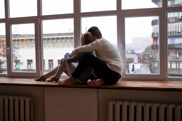 Casal jovem feliz senta-se perto da janela na sala