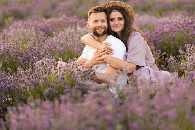 Casal jovem feliz tendo um encontro romântico no campo de lavanda sentado e abraçando