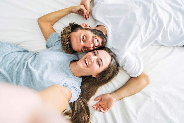 Casal jovem feliz tirando retrato selfie com celular inteligente deitado na cama