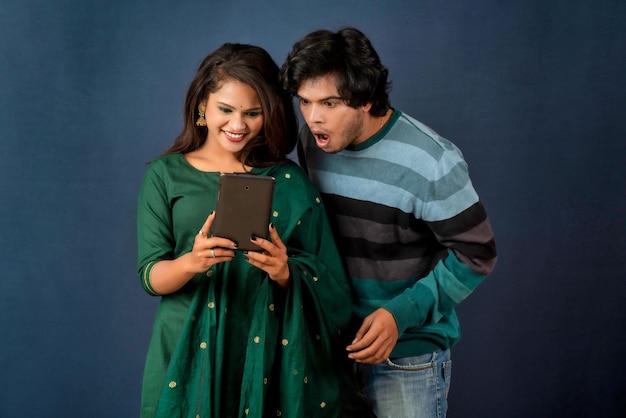 Casal jovem feliz usando celular e mostrando uma tela em branco de um smartphone ou celular ou tablet em um fundo cinza