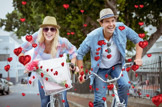 Casal jovem hip indo para um passeio de bicicleta contra balões de coração vermelho flutuando