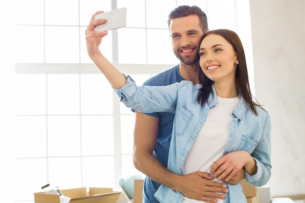 Casal jovem, homem e mulher, se mudando para um novo apartamento juntos, realocação usando um dispositivo digital