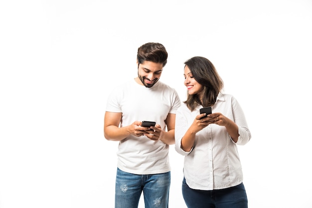 Foto casal jovem indiano usando smartphone ou aparelho celular, isolado sobre um fundo branco ou de tijolo vermelho