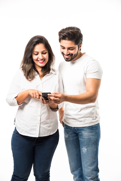 Casal jovem indiano usando smartphone ou aparelho celular, isolado sobre um fundo branco ou de tijolo vermelho