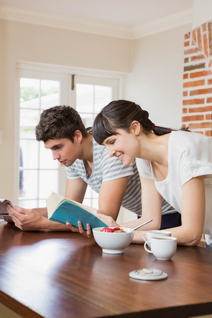 Casal jovem lendo livro enquanto tomando café na cozinha