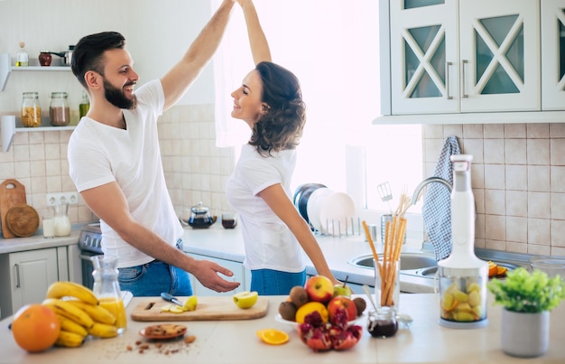 Casal jovem lindo e animado, apaixonado, cozinhando na cozinha e se divertindo juntos, enquanto dançam e sorriem