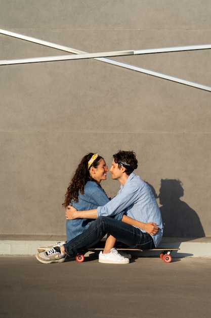 Casal jovem na moda senta-se no longboard na rua da cidade ensolarada feliz e sorridente. Abraço e aproveite o tempo juntos