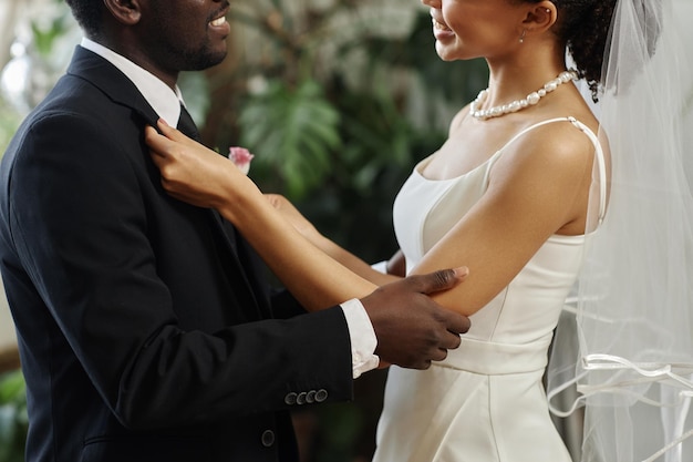 Casal jovem negro se casando com a noiva ajustando jaqueta e flor na lapela