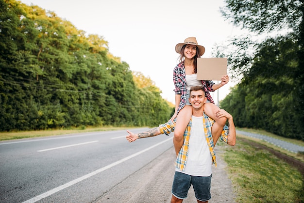 Casal jovem pedindo carona com papelão vazio