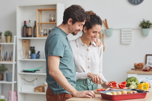 Foto casal jovem preparando comida juntos na cozinha preparando um prato de vegetais