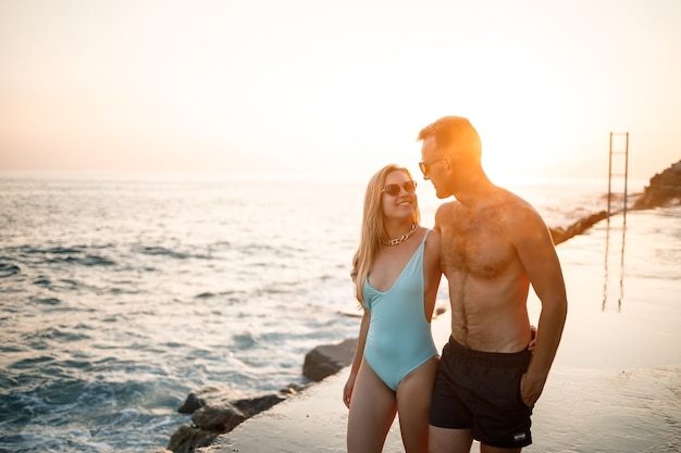 Casal jovem romântico apaixonado caminhando juntos ao pôr do sol ao longo da praia do Mediterrâneo. Férias de verão em um país quente. Casal feliz de férias na Turquia. Foco seletivo