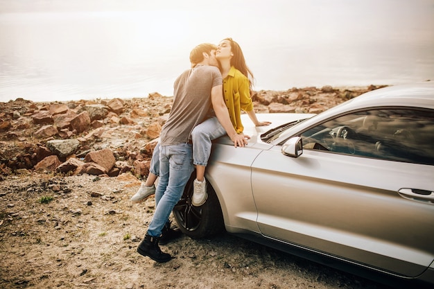 Casal jovem romântico compartilhando um momento especial ao ar livre. jovem casal apaixonado em uma viagem. casal se abraçando enquanto está sentado no capô do carro na natureza