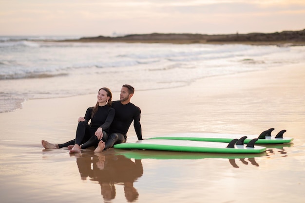 Casal jovem romântico relaxando na praia após o dia de surf