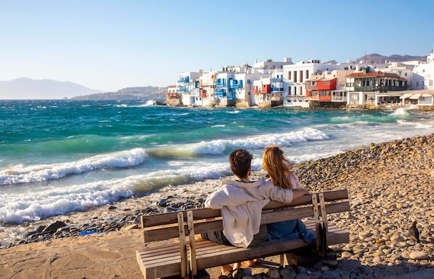 Casal jovem romântico sentado contra as ondas ilha de mykonos grécia famosa área de little venice da cidade de mykonos