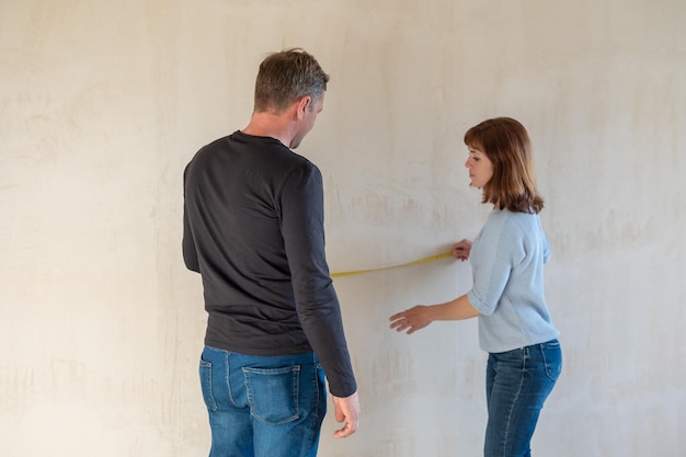 Foto casal jovem se mudando para um novo apartamento as pessoas medem o tamanho da parede com fita métrica conceito novas casas novo começo