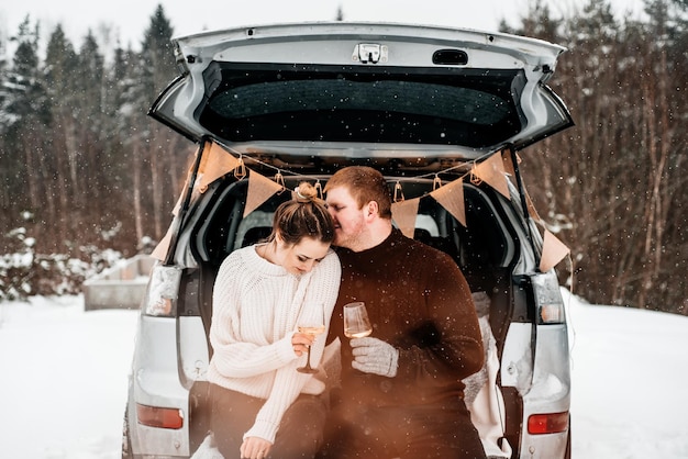 Casal jovem segurando copos de vinho de pé ao lado do carro durante o inverno