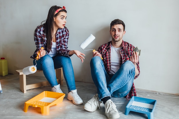 Foto casal jovem segurando os rolos de pintura e sorrindo um ao outro enquanto descansava durante a reparação