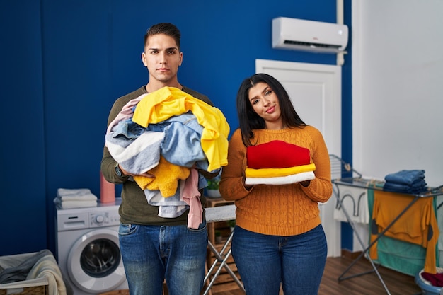 Foto casal jovem segurando roupa suja e roupa limpa relaxada com expressão séria no rosto. olhar simples e natural para a câmera.