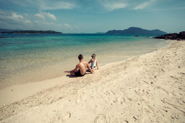 Casal jovem sensual em trajes de banho deitado na areia à beira-mar, sobre o céu e o fundo da ilha tropical. Phuket. Tailândia.