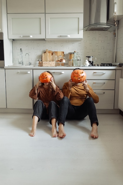 Casal jovem sentado no chão da cozinha segurando abóboras de Halloween