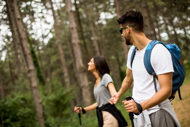 Casal jovem sorridente andando com mochilas na floresta em um dia de verão