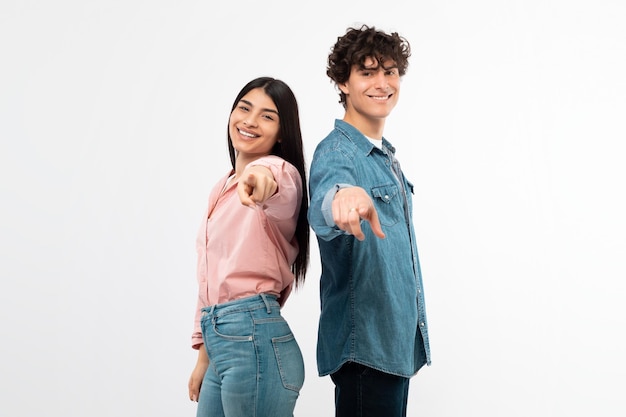 Casal jovem sorridente apontando os dedos para a câmera no fundo branco