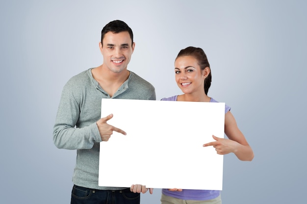 Casal jovem sorridente apontando para a placa que estão segurando contra a vinheta cinza