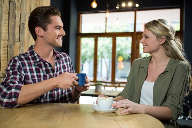 Casal jovem sorridente, conversando enquanto toma um café na mesa do refeitório