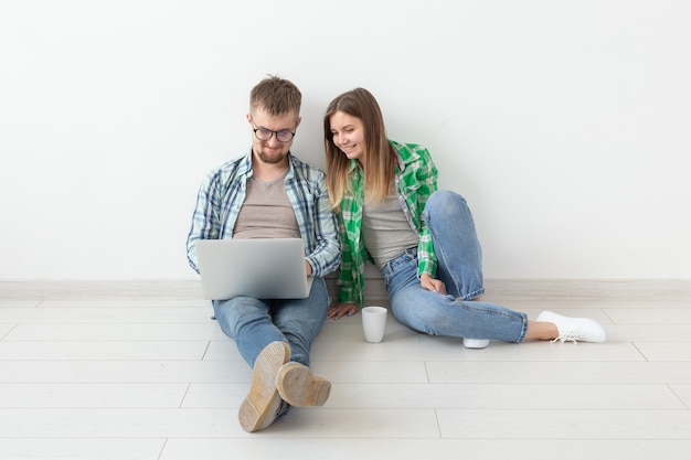 Casal jovem sorridente faz compras online de móveis em seu novo apartamento hipotecário. Conceito de compra online com laptop e gadgets. Copyspace