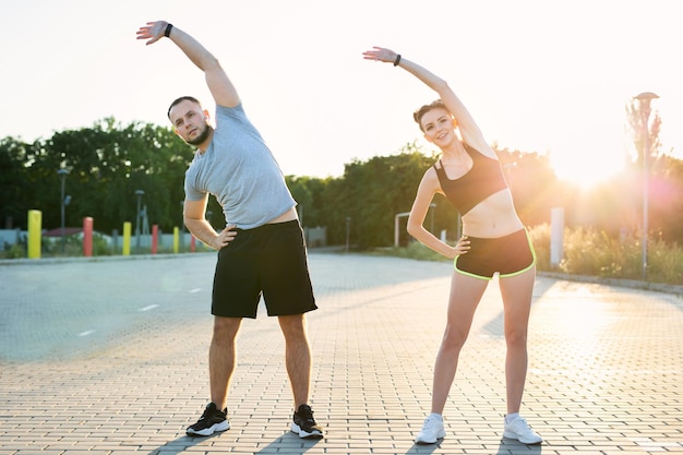 Casal jovem treina ao ar livre em um parque no verão ao pôr do sol