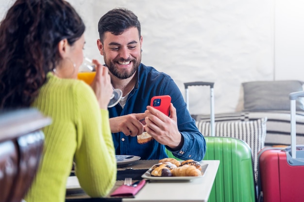 Casal jovem turista olhando para o telefone e tomando café da manhã em um restaurante de hotel