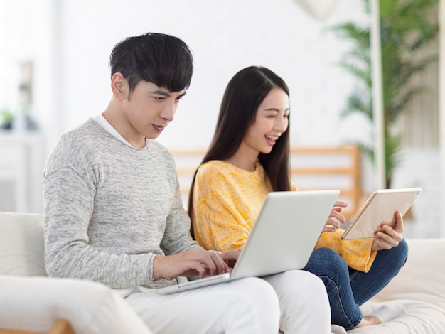 Casal jovem usando laptop para escritório e assistindo filmes no sofá em casa