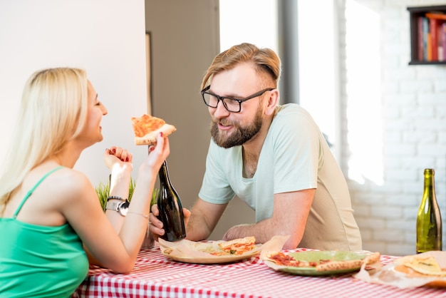 Casal jovem vestido de forma casual almoçando com pizza e cerveja em casa